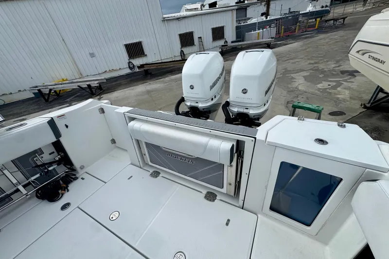 Slide: The Image of 2023 Blackfin 332 CC boat with dual Mercury outboard engines, docked near a warehouse. - 105