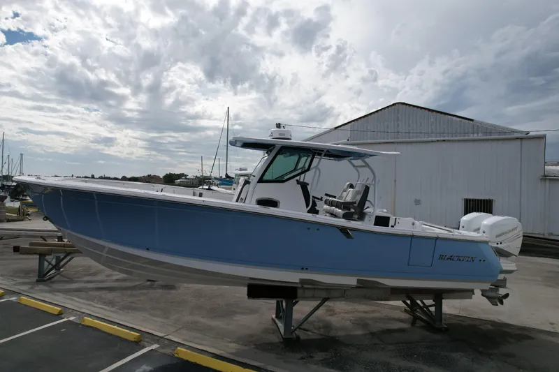 Slide: The Image of 2023 Blackfin 332 CC boat displayed outdoors on a stand under cloudy skies. - 25
