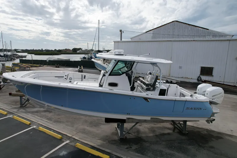 Slide: The Image of 2023 Blackfin 332 CC boat on display at a marina, featuring sleek design and twin engines. - 26