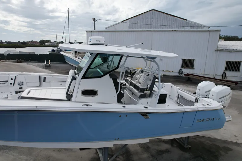 Slide: The Image of 2023 Blackfin 332 CC boat with blue hull, docked near a warehouse. - 28