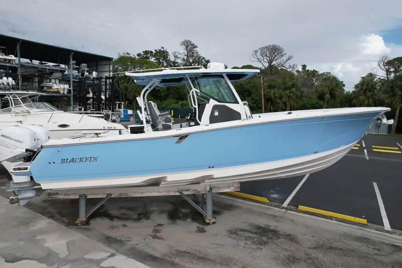 Slide: The Image of 2023 Blackfin 332 CC boat in light blue, displayed on a stand in a marina. - 42