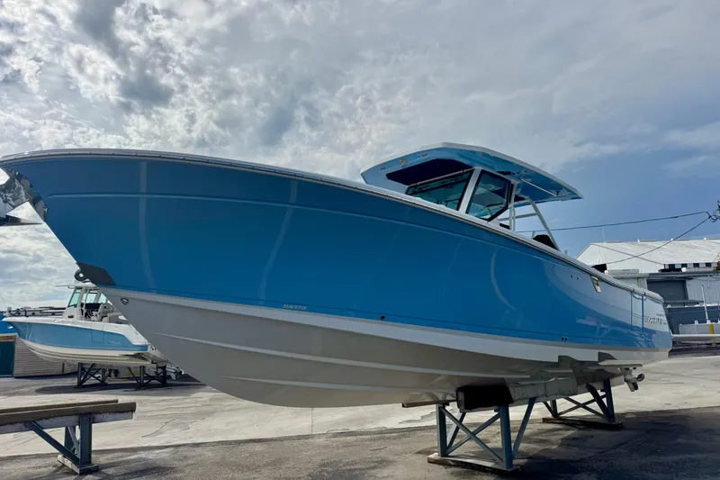 Slide: The Image of 2023 Blackfin 332 CC boat in vibrant blue, displayed on a stand under a cloudy sky. - 51