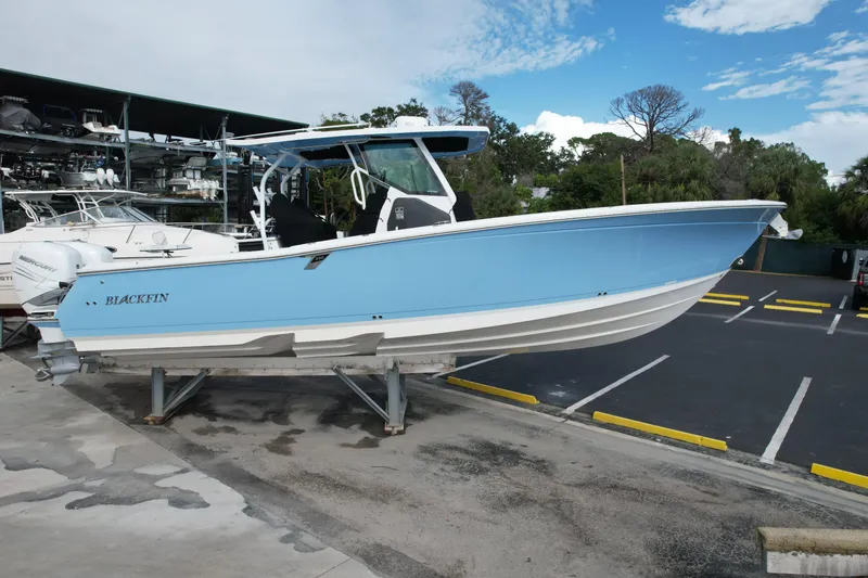 Slide: The Image of 2023 Blackfin 332 CC boat in light blue, displayed on a stand in a marina. - 7