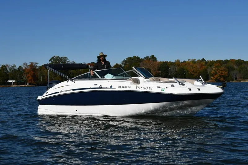 Slide: The Image of 2016 Hurricane SunDeck 2200 DC OB boat cruising on a lake with autumn trees in the background. - 2
