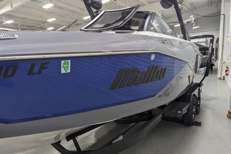 Slide: The Image of 2023 Malibu Wakesetter 25 LSV boat in showroom, featuring sleek blue and gray design. - 18