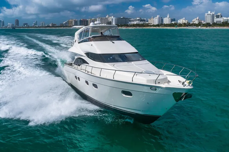 Slide: The Image of Luxurious 2005 Marquis 59 yacht cruising on turquoise waters near a city skyline. - 0