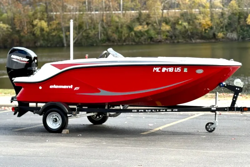 Slide: The Image of 2022 Bayliner Element M15 boat in vibrant red on a trailer by a river. - 1