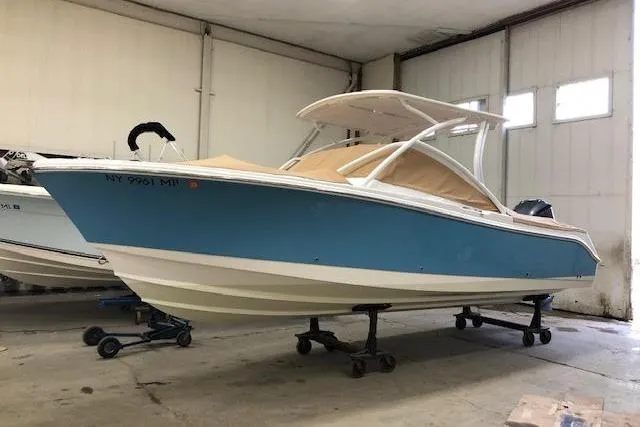 The Image of 2018 Edgewater 248CX Crossover boat in storage, blue hull, white interior, on stands. - 1