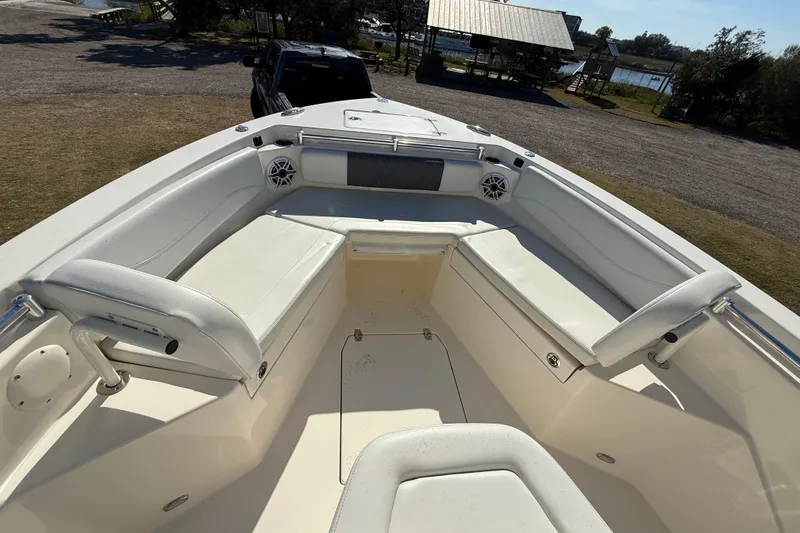 Slide: The Image of 2023 Cobia 240CC boat interior with white seating and speakers, parked near a lake. - 23