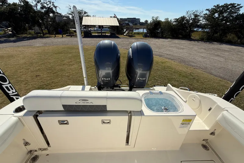Slide: The Image of 2023 Cobia 240CC boat with dual 150 engines and a livewell, parked on grass. - 28