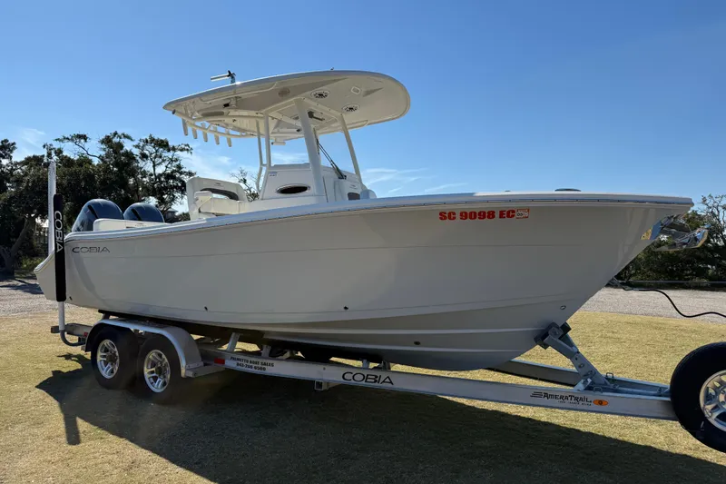 Slide: The Image of 2023 Cobia 240CC boat on trailer, parked on grass under clear sky. - 3