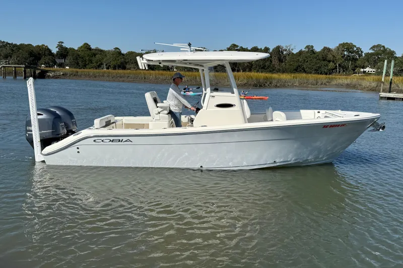 Slide: The Image of 2023 Cobia 240CC boat on calm water, side view with trees in the background. - 9