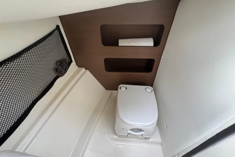 Slide: The Image of 2015 Sea Ray 220 Sundeck Outboard interior with compact marine toilet and storage shelves. - 32