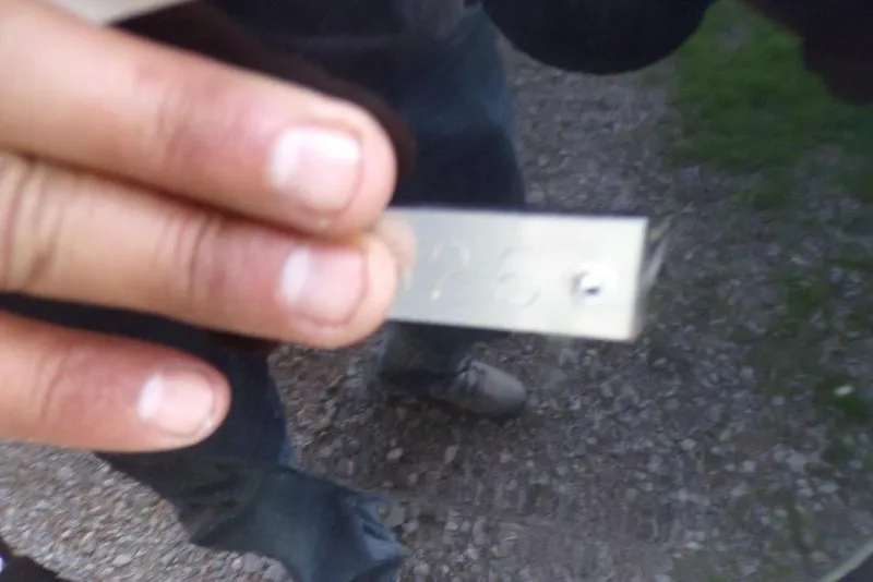 Slide: The Image of Hand holding a metal tag with engraved numbers, outdoors on gravel path. - 5