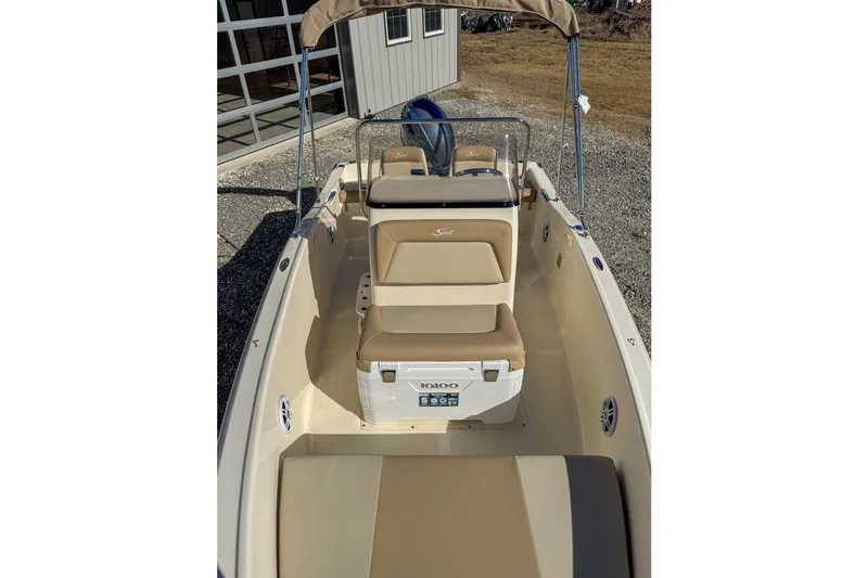 Slide: The Image of 2026 Scout 175 Sportfish boat interior with beige seating and cooler, docked outdoors. - 19