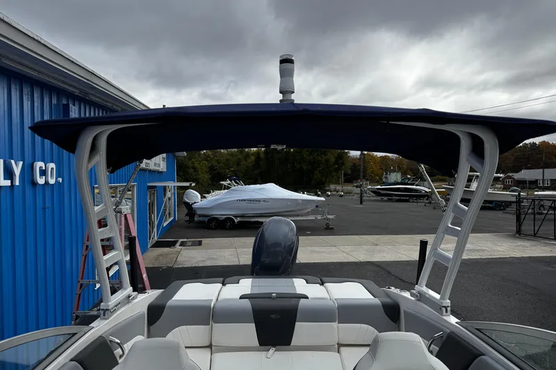 Slide: The Image of 2023 Chaparral 21 SSi OB boat with canopy, parked near blue building under cloudy sky. - 17