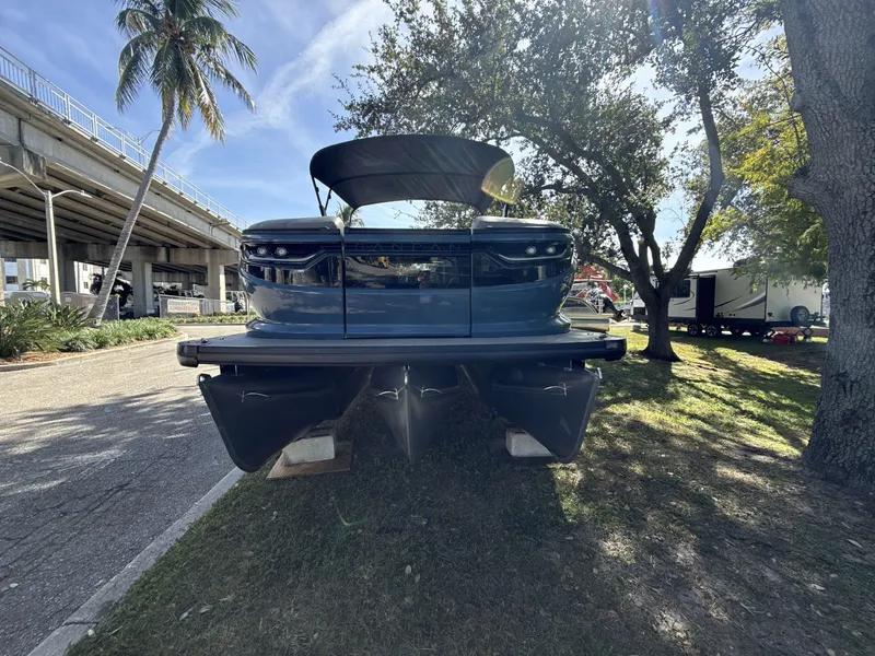 Slide: The Image of Sanpan 2500 MTF 2026 pontoon boat on display under trees, near a bridge. - 7