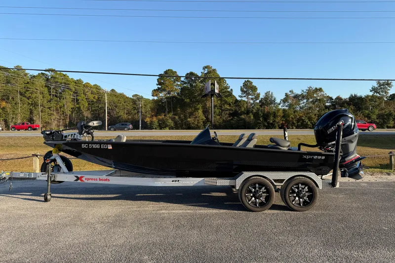 The Image of 2025 Xpress X21 Pro boat on trailer, parked roadside with trees in background. - 1