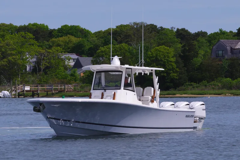 Slide: The Image of 2025 Regulator 35 boat cruising on a calm lake with lush green shoreline. - 5