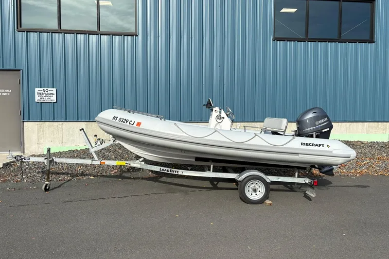 Slide: The Image of 2024 Ribcraft 4.8T inflatable boat on trailer, parked by blue industrial building. - 16
