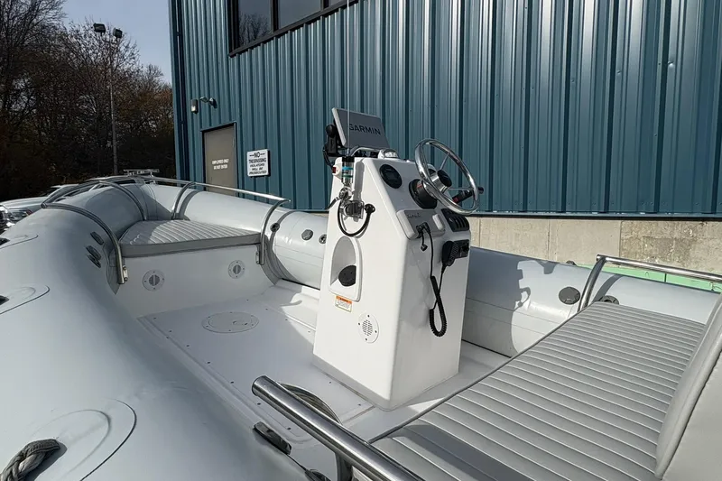 Slide: The Image of 2024 Ribcraft 4.8T boat interior with steering console and seating, docked near blue building. - 2