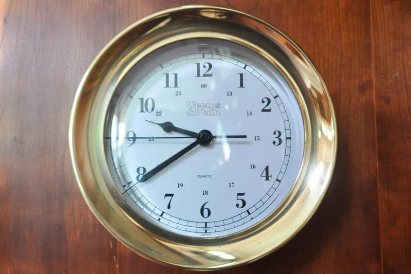 Slide: The Image of Brass wall clock with white face and black numerals on wooden background. - 63