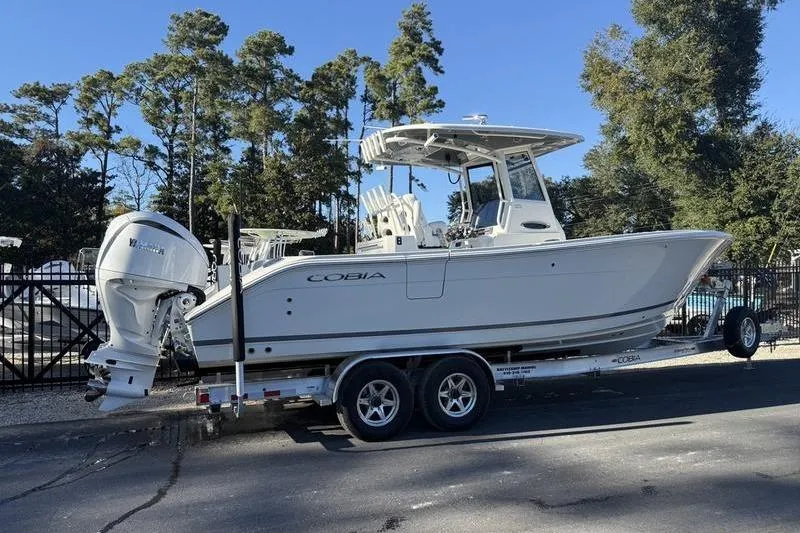 Slide: The Image of 2026 Cobia 265 Open Center Console boat on trailer, parked outdoors. - 2