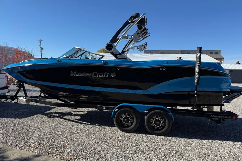 Slide: The Image of 2019 MasterCraft X24 boat on trailer, blue and black design, parked outdoors. - 2