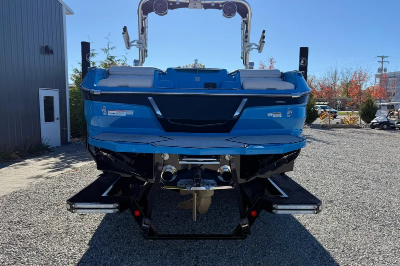 Slide: The Image of 2019 MasterCraft X24 boat, blue exterior, rear view, parked on gravel. - 3