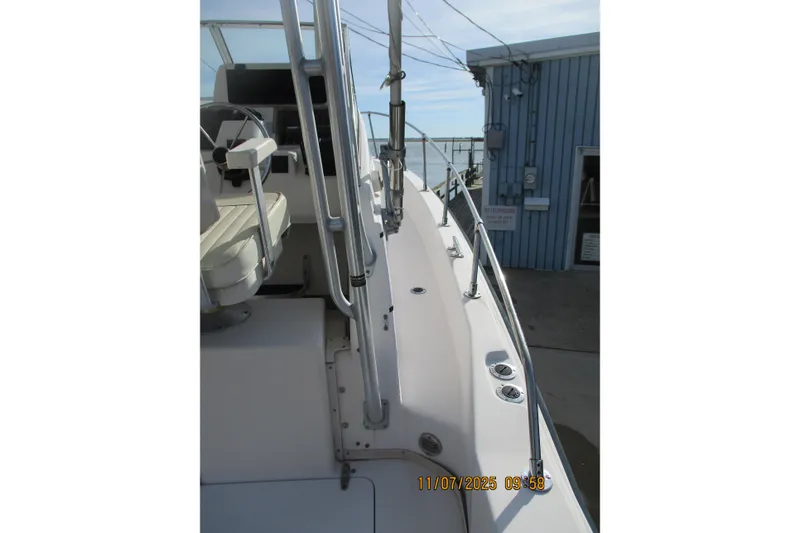 Slide: The Image of 1996 Grady-White Sailfish 272 boat deck with railing and seating, docked near a blue building. - 26