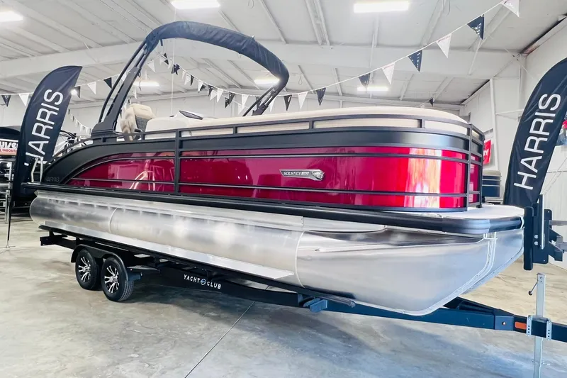 The Image of 2025 Harris Solstice 250 pontoon boat displayed indoors with banners and trailer. - 0