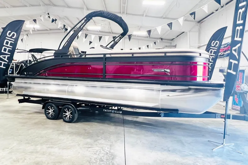 Slide: The Image of 2025 Harris Solstice 250 pontoon boat on display in a showroom with banners. - 6