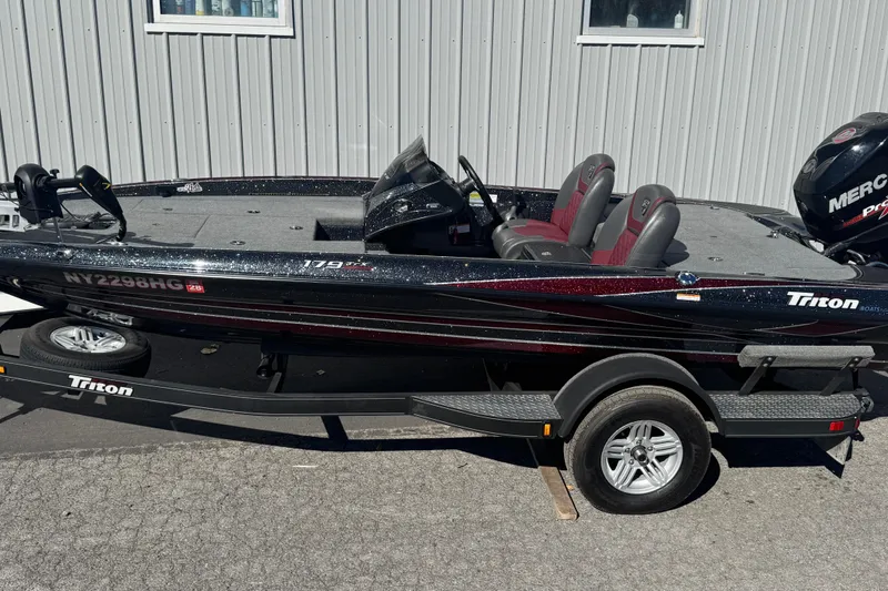 Slide: The Image of 2016 Triton 179 TrX boat on trailer, parked outdoors, featuring dual seats and Mercury engine. - 2