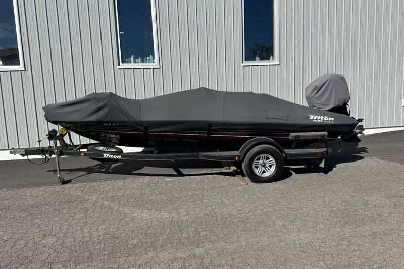 Slide: The Image of 2016 Triton 179 TrX boat covered on trailer, parked beside a building. - 4