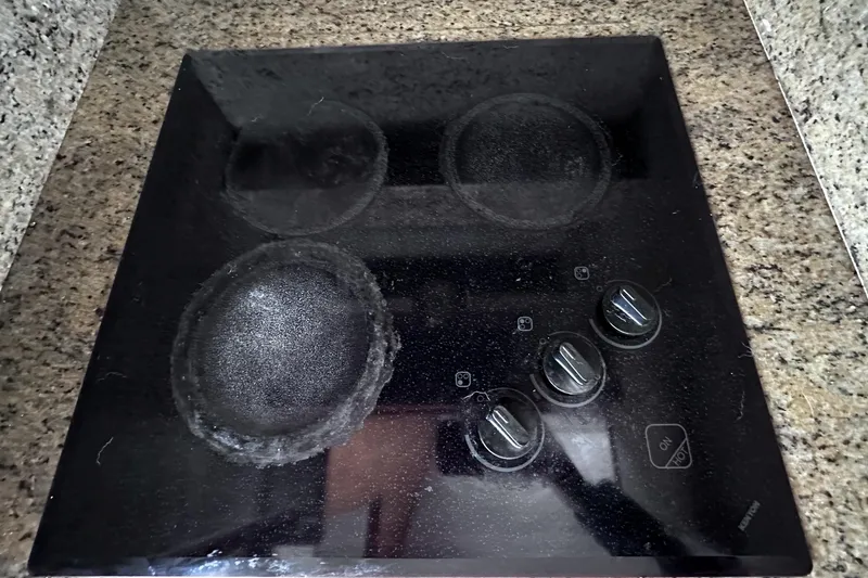 Slide: The Image of Black stovetop with four burners and control knobs on a granite countertop. - 38