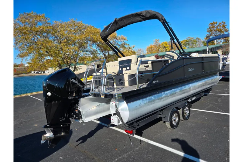 Slide: The Image of 2021 Barletta C24UC pontoon boat with Mercury outboard motor, parked near a lake. - 2