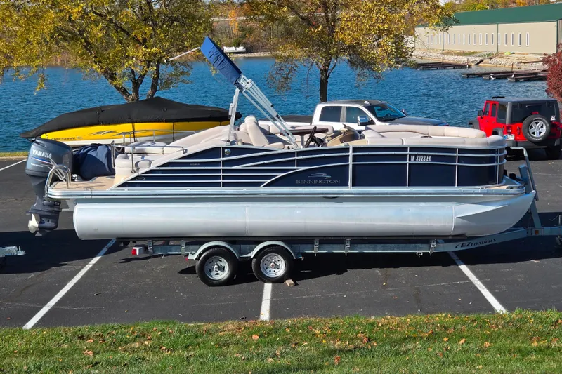 The Image of 2011 Bennington 2275RCW OB pontoon boat on trailer in parking lot by lake. - 0
