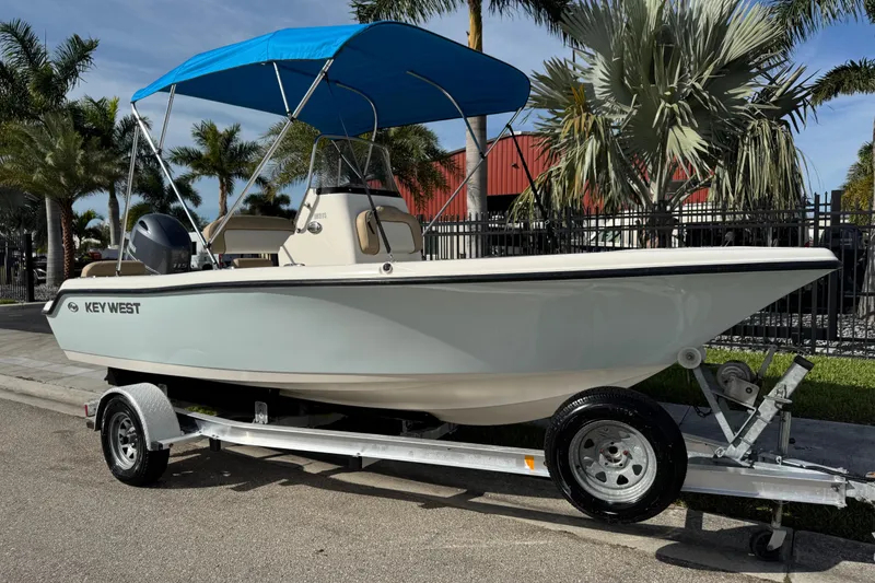 Slide: The Image of 2017 Key West 189 FS boat on trailer with blue canopy, parked near palm trees. - 0