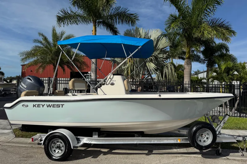 Slide: The Image of 2017 Key West 189 FS boat with blue canopy on trailer, surrounded by palm trees. - 1