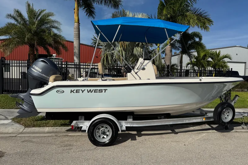 Slide: The Image of 2017 Key West 189 FS boat with blue canopy on trailer, parked near palm trees. - 2
