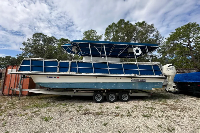 Slide: The Image of 1999 Catamaran Coaches 31 boat with blue canopy on a trailer, parked outdoors. - 0