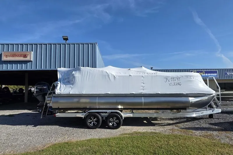Slide: The Image of 2026 Veranda Vista 22RC pontoon boat covered, parked on a trailer outside a dealership. - 7