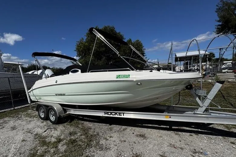 The Image of 2022 Stingray 212SC boat on a trailer, parked outdoors under a clear blue sky. - 1