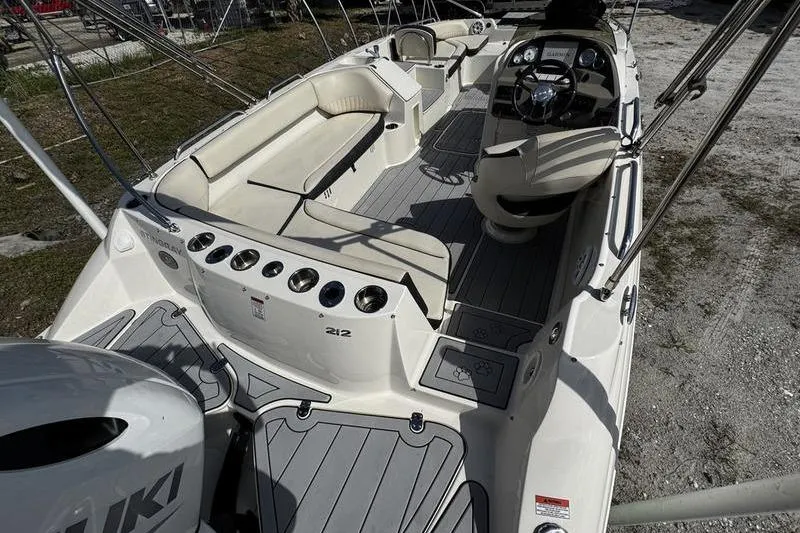 Slide: The Image of 2022 Stingray 212SC boat interior with seating and steering console, parked on land. - 26