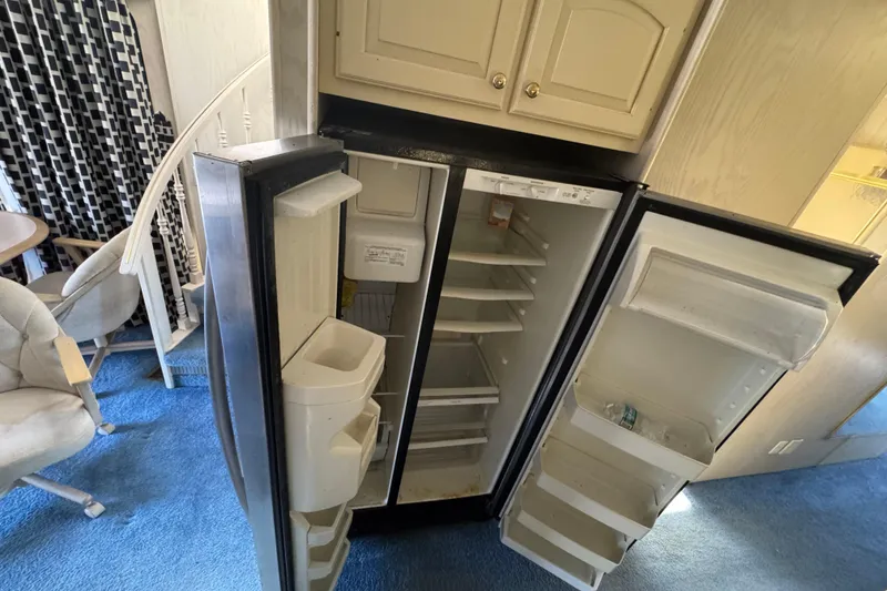 Slide: The Image of Open refrigerator inside 1997 Monticello River Yacht, showing empty shelves and blue carpeted floor. - 8