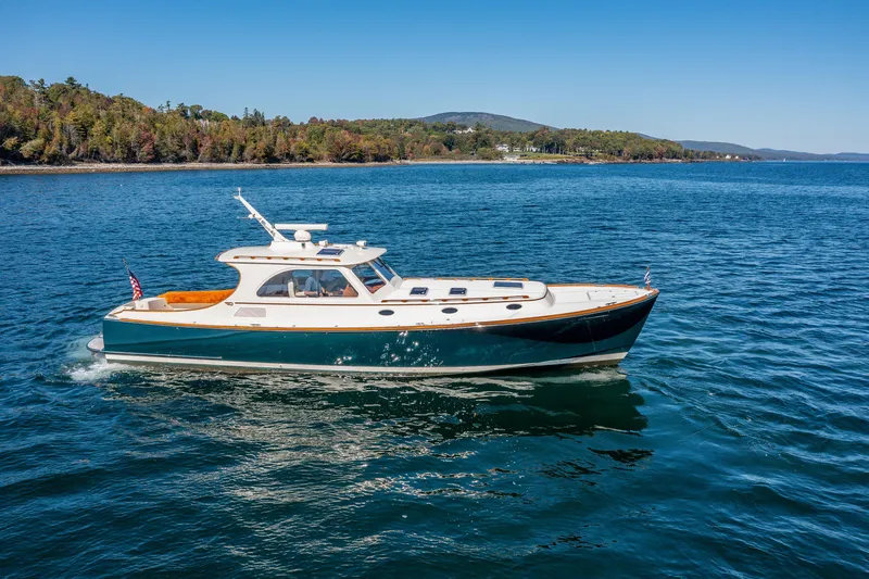 Slide: The Image of 2002 Hinckley Talaria 44 Express yacht cruising on a serene lake with forested shoreline. - 16