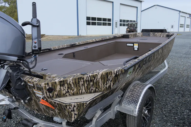 Slide: The Image of 2026 Avid 16 Commander boat with camouflage design on a trailer near industrial buildings. - 5