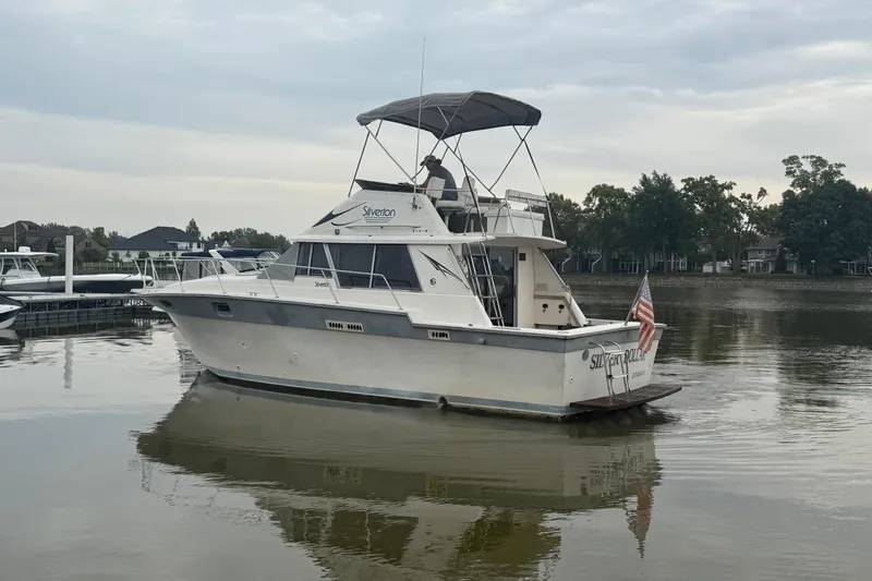 Slide: The Image of 1986 Silverton 34 Convertible boat on calm water, featuring an American flag. - 24