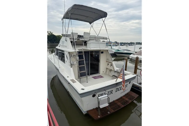 Slide: The Image of 1986 Silverton 34 Convertible boat docked, featuring a canopy and American flag. - 7