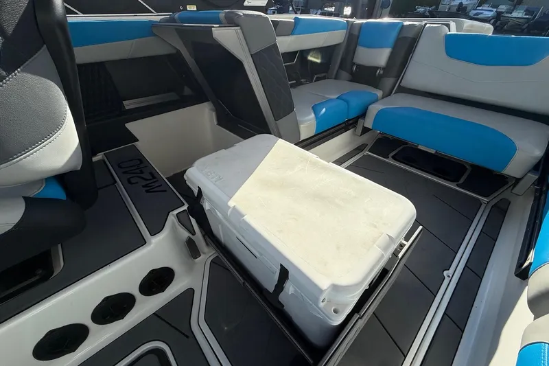 Slide: The Image of 2023 Malibu M240 boat interior with blue and gray seating, featuring a central cooler. - 21